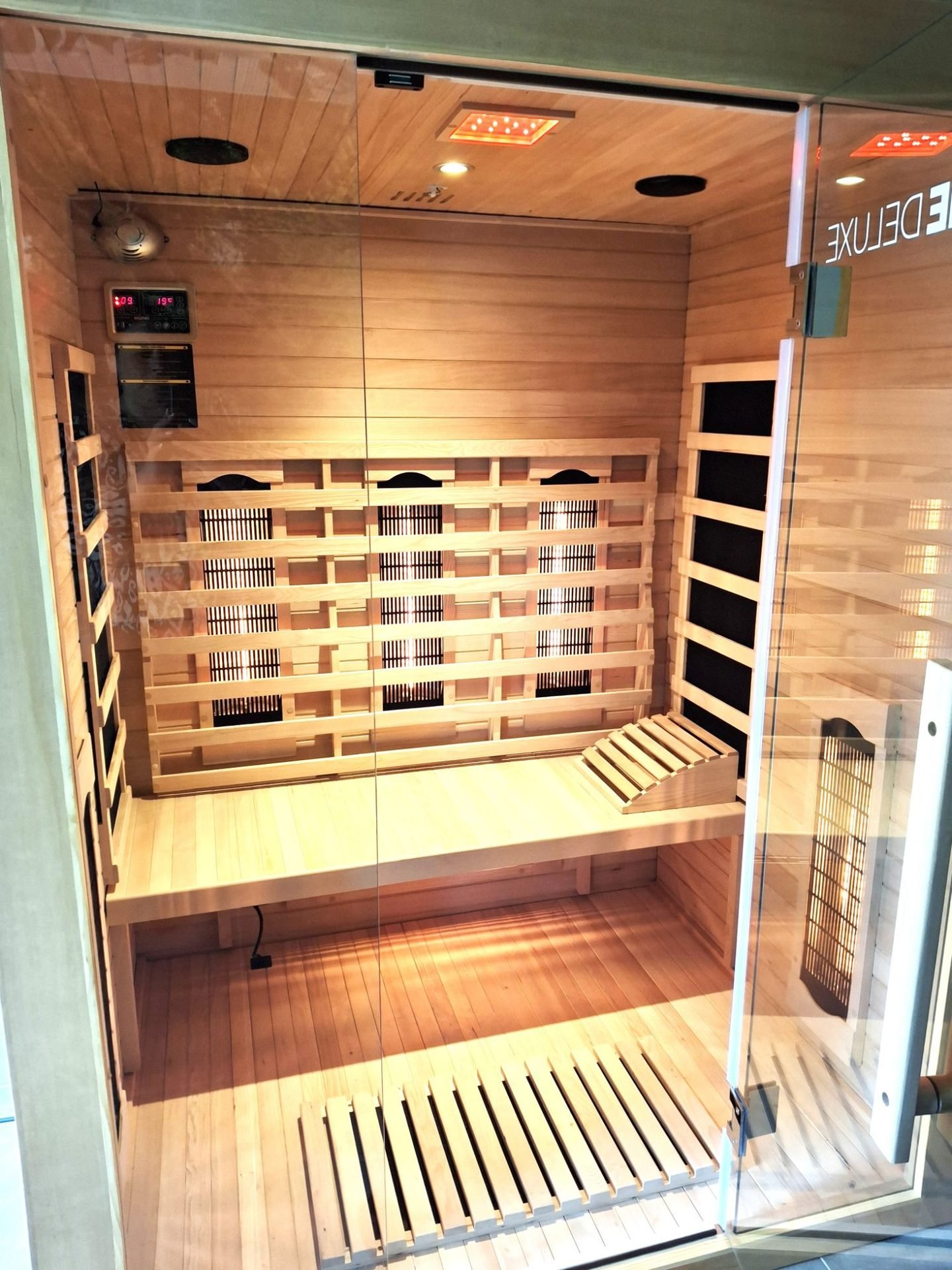 Intérieur du sauna : banc en bois clair, appui-tête et panneaux chauffants éclairés